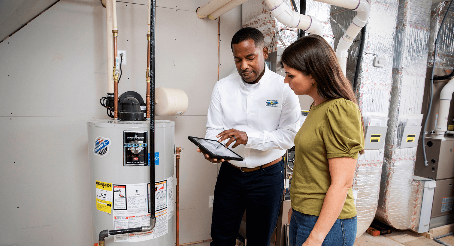 A Performance plumber using a tablet to discuss residential water heater services, repairs, and replacement options with a homeowner.