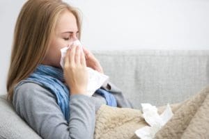 A woman blowing her nose into tissues : Can My Air Conditioner Make Me Sick? Air conditioning sickness symptoms